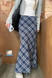 Person wearing a blue plaid skirt in front of a brick wall.