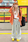 Person wearing an orange plaid shirt, white pants, and yellow shoes standing in front of a train.
