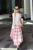 Woman in a white top and red plaid skirt walking outdoors.