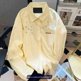 Yellow shirt with floral embroidery on a chair with magazines in the background