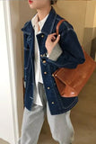 Person wearing a denim jacket holding a brown leather handbag indoors.