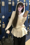 Person wearing a white knit sweater with a hood, holding a phone and a black bag, in front of blue lockers.