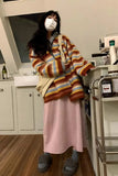 Person wearing a colorful striped sweater and pink skirt in a kitchen.