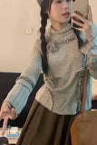 Person taking a mirror selfie wearing a light gray sweater with decorative elements.