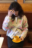 Woman in a floral cardigan holding a yellow cup and saucer in a cafe.