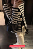 Person wearing a black and white striped cardigan with a blue handbag indoors.