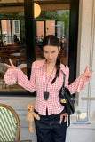 Woman wearing a pink checkered shirt with a teddy bear and black bag in an outdoor setting.