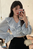 Woman taking a mirror selfie wearing a light blue blouse with ruffled details.