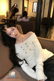 Woman in a white off-shoulder sweater sitting on a couch in a room with mirrors.
