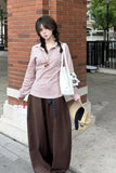 Woman in striped shirt and wide-leg pants standing against a brick wall.