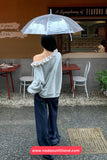 Person holding a transparent umbrella in an outdoor setting with tables and chairs.