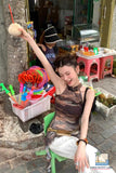 Woman sitting on a chair holding a coconut drink with a child in the background.