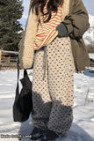 Person wearing a long coat, patterned pants, and striped shirt in a snowy landscape.