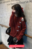 Woman in a red sweater with bow details leaning against a wall, holding a coffee cup.