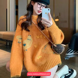 Person wearing a mustard yellow sweater with floral patterns, taking a selfie indoors.