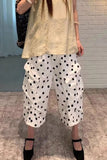 Person wearing a beige top and white polka dot pants against a brick wall.