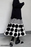 Person wearing a black and white polka dot skirt with a plain background