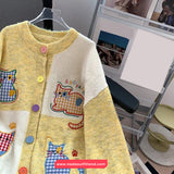 Yellow cardigan with cat designs on a hanger in front of a computer screen.