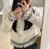 Person wearing a white cardigan with black polka dot and checkered trim, taking a mirror selfie.