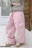 Person wearing a gray puffer jacket and pink checkered pants standing in the snow.