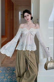 Woman wearing a white off-shoulder blouse and green pants in an indoor setting.