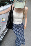 Person wearing a white tank top and blue plaid skirt standing next to a car.