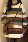 Person wearing a colorful striped sweater holding a brown bag indoors.