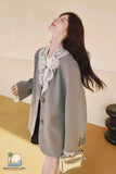Woman wearing a gray blazer with lace details and holding a gold handbag indoors.