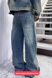 Person wearing oversized blue jeans standing on a staircase with a visible brand logo at the bottom.