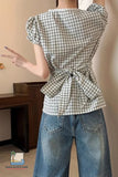 Person wearing a green and white checkered blouse with puffed sleeves and tied waist, paired with blue jeans.