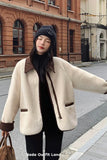 Woman wearing a cream coat with brown accents on a city street.