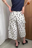Person wearing a navy polka dot top and white pants with black polka dots, standing against a wooden door.