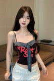Woman wearing a black top with pink text and denim accents, standing indoors.