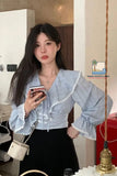 Woman taking a mirror selfie wearing a light blue blouse with ruffled sleeves.