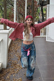 Person wearing a red plaid shirt and blue jeans with a pink object, standing on a patio with trees and a white structure in the background.
