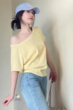 Woman wearing a yellow off-shoulder top and blue jeans against a plain background