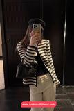Person wearing a black and white striped sweater, white pants, and a black beret taking a mirror selfie.