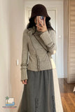 Person wearing a gray knitted cardigan and skirt in a room with wooden flooring.