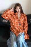 Person wearing an orange plaid shirt and blue jeans sitting on a black couch.