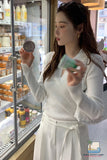 Woman in a white outfit holding a product in front of a refrigerator display.