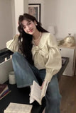 Woman sitting on a couch in a living room, wearing a light-colored blouse with a bow and blue jeans.