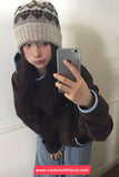 Person wearing a brown jacket and knit hat taking a mirror selfie.