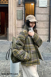 Person wearing a plaid coat and beige hat taking a selfie outdoors.