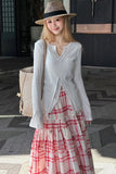 Woman wearing a white top and red plaid skirt with a straw hat, standing indoors.