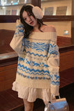 Woman wearing a white and blue patterned sweater with matching gloves indoors.