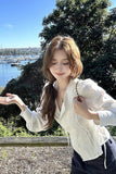 Woman in a white blouse standing outdoors with water and trees in the background