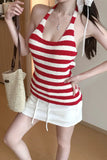 Woman wearing a red and white striped tank top and white shorts, holding a straw bag indoors.