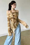 A woman modeling a long-sleeve, off-the-shoulder top with a brown and beige tie-dye pattern, paired with light blue wide-leg jeans, in an indoor setting.