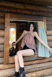 Woman sitting on a wooden porch holding a black handbag and a green and white checkered bag.