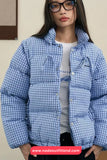 Person wearing a blue checkered puffer jacket with a neutral background